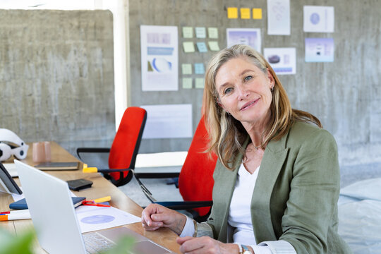 Woman reviewing charts at modern office desk, with laptop, coffee mug, copy space