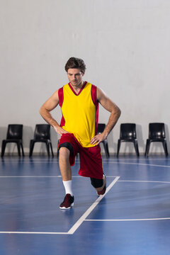 Man performing forward lunge stretch on indoor basketball court, with black chairs and white lines