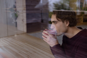 Woman sipping coffee at modern coffee shop window with red mug and wooden tables, copy space