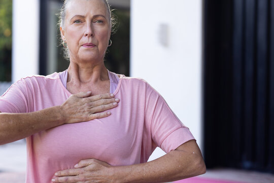 Senior woman practicing breathing exercise on modern outdoor patio, with pink yoga mat