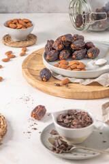 Medjool dates, almonds and spoonful of shredded coconut on a plate with a wooden board, surrounded by scattered almonds, dates, and chocolate chunks, creating a rustic and appetizing scene