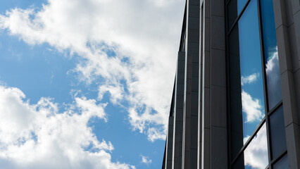 Contemporary glass facade of office building reflecting bright blue sky and clouds, urban architecture concept.