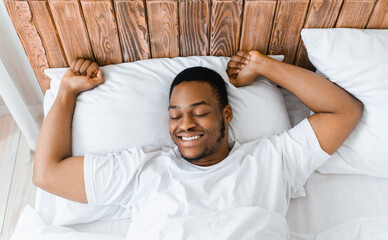 Rested African American Man Waking Up Stretching Hands Awakening Lying In Bed At Home In The...