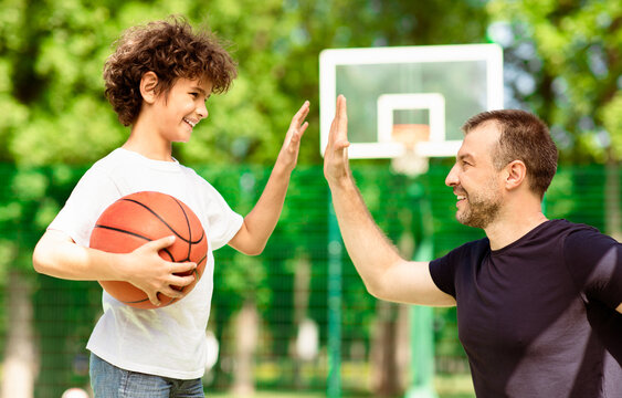 Greetings. Adult coach giving high five to kid with ball at playing field, blurred background