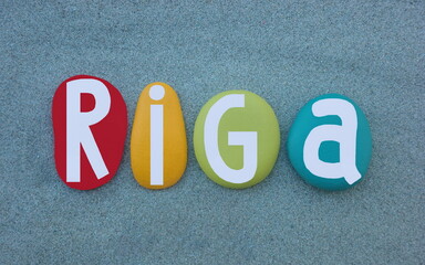 Riga, capital and largest city of Latvia, creative souvenir or logo composed with multi colored hand painted stone letters over green sand