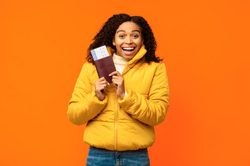 Obraz premium Joyful African American Traveler Woman Holding Flight Tickets Smiling To Camera Standing Over Yellow Studio Background. Winter Travel And Vacation, Tourism Concept