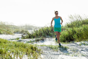 A woman runs on a coastal beach showing an active 
healthy lifestyle while getting cardio. 