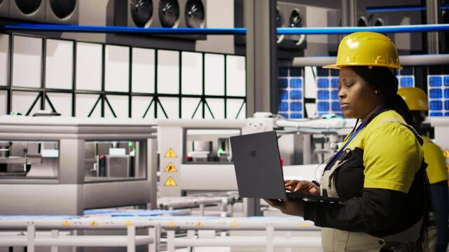 Engineer walking in smart factory, using laptop to analyze IoT sensors data, refining gear efficiency. Industry 4.0 plant expert performing system diagnostics to reduce downtime, camera A