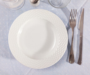 Clean empty ceramic plate with knife and fork on a tablecloth in a restaurant