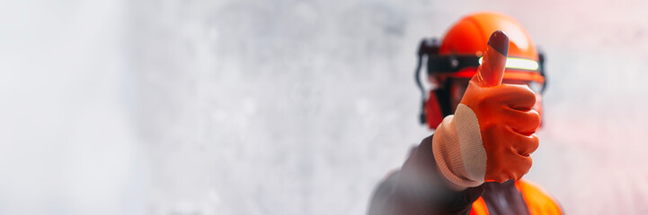 A construction worker in a helmet and protective gloves shows a thumbs up. Concept approval and success in repair and construction.
