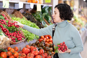 Portrait of female shopper choosing ripe tomatoes at supermarket counter