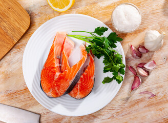 Fresh uncooked salmon fish with greens and lemon on a ceramic plate with kitchen knife