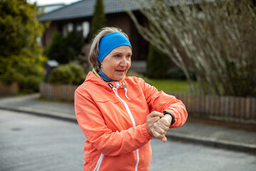 Senior caucasian woman using a smartwatch while out exercising and jogging on a sidewalk in the suburbs