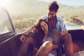 Young mixed couple on a date in a truck bed of an old timer truck on a road trip on a sandy beach near the ocean