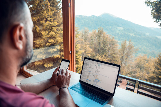 Man checking smartphone with chart growth and laptop while working in mountain cabin with scenic view