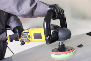 Man polishing car hood with orbital polisher indoors, closeup