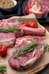 Pieces of raw beef, rosemary and tomatoes on table, closeup