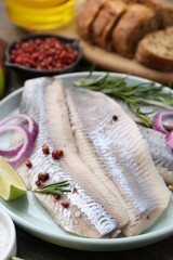 Marinated herring fillets with onion rings, rosemary, lime and peppercorns on table, closeup
