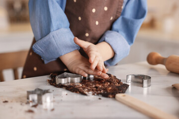 Cooking recipe. Little girl cutting cookie dough with cutters at table indoors, closeup