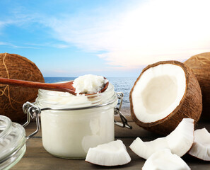 Cooking oil in jar and coconuts on wooden table against sea