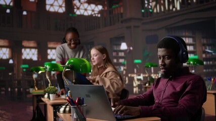 Young adult listening to study music and writing ideas for bachelor paper, using ambient sounds to help with concentration in the campus library. Girl student does academic research. Camera B.