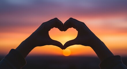 Hands framing the sun in a heart shape against a vivid colorful sunset.