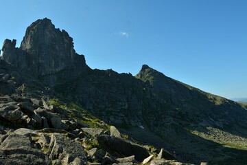 A ridge of high cliffs casts a shadow from the rising sun over a picturesque valley on a sunny summer day.