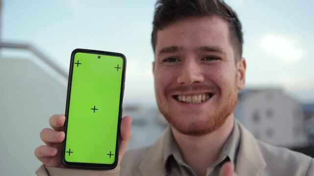 Man showcasing the capabilities of his smartphone while standing on a balcony at a business center. With a green screen and tracking dot, the phone is perfect for social networks, email, and