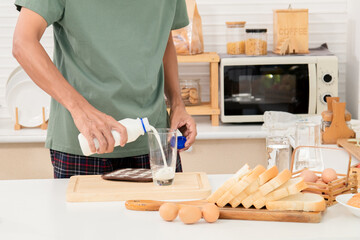 Asian beard man active strong man pouring fresh pure milk into glass in morning, male drink milk in cup after wake up for health and wellbeing in kitchen. Enjoying refreshing drink for breakfast.