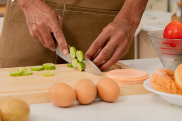Asian man with beard sitting makes sandwich for breakfast in morning at kitchen. Male wear apron enjoy make food for health care in house,  free time in modern kitchen interior. healthy food at home.