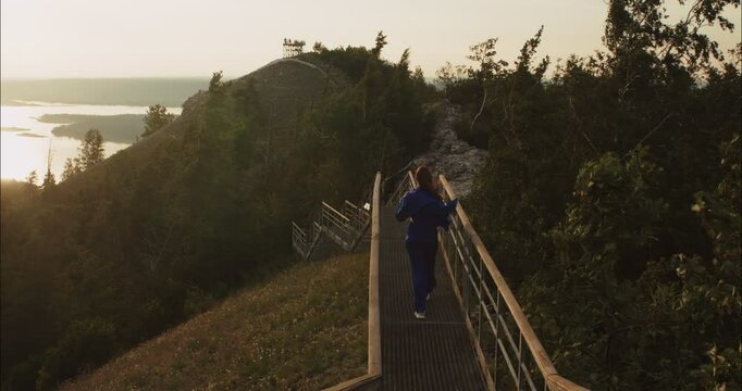 Woman walking down metal staircase on mountain at sunset