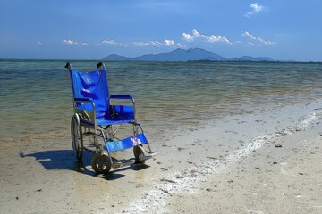 Empty wheelchair on a beach under a clear blue sky.