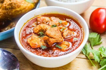 a bowl of chicken curry dish on a wooden table with vegetables