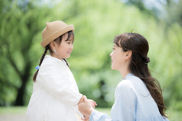 Close-up of an image of parent and child (mother and daughter) looking at each other with beautiful fresh greenery in the background, raising a child and loving each other.