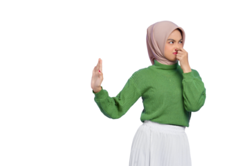 Beautiful annoyed Asian woman in green sweater makes stop gesture, covering her nose with hand isolated on transparent background