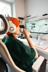 Gamer girl enjoying drink in modern tech corner, wearing orange beanie and white headphones....