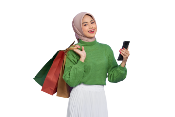 Cheerful beautiful Asian woman in green sweater holding shopping bags, using mobile phone looking at camera isolated on transparent background