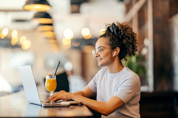 Profile view of interracial freelancer sitting in coffee shop and typing report on laptop.