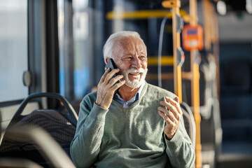 Portrait of happy senior man riding public transportation and talking on his cellphone.