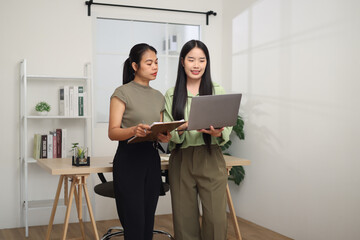Portrait of Two Asian business woman standing in an office, holding documents and discussing work. Business ideas and strategies