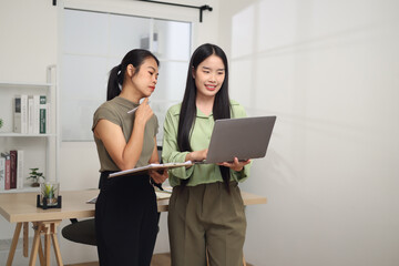 Portrait of Two Asian business woman standing in an office, holding documents and discussing work. Business ideas and strategies
