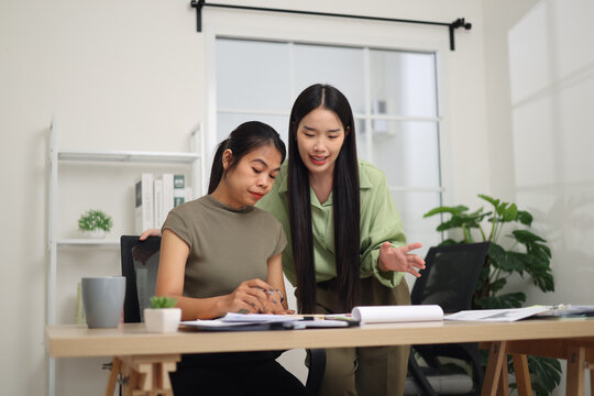 Portrait of Two female colleagues are working together in an office. One stands explaining the work, while the other sits and listens with interest.