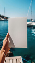 Obraz premium Blank White Brochure Held by a Person Near a Marina With Yachts and Clear Blue Sky 