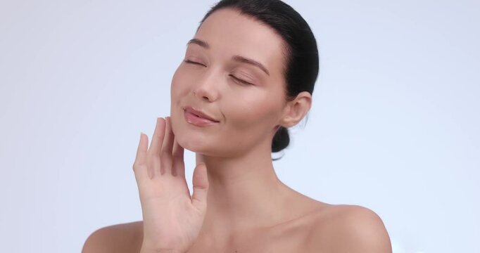 Caucasian woman smiles gently while caressing her face in a clean studio. Ideal for dermatology ads, anti-aging skincare, facial rejuvenation services, and clinical beauty campaigns.