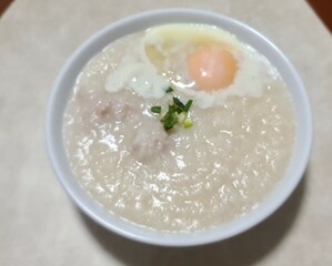 pork and rice porridge with soft boiled egg in white bowl on table