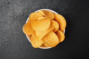 Crispy potato chips in a white bowl on a dark countertop