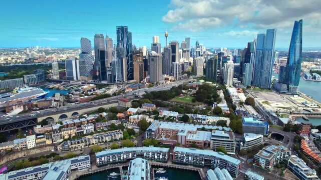 Aerial footage of Sydney CBD featuring iconic skyscrapers, bustling harbor, busy highways, and historic The Rocks district. Stunning cityscape under clear blue skies.