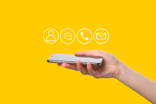 A hand holding a smartphone displays contact icons against a bright yellow backdrop