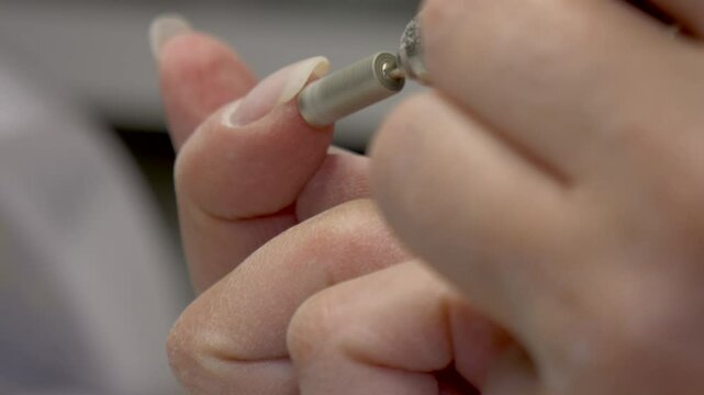 Closeup shot of a woman doing her nail with an electric nail drill machine, with blurred background