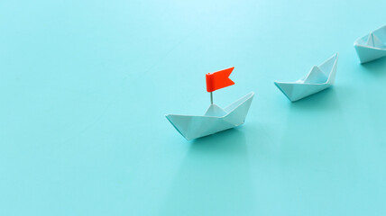 Paper boats following ahead of the leader with red flag